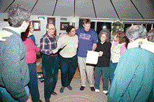 photo of what is apparently the goodbye party at Highlander. People gather in a circle, hugging and singing.