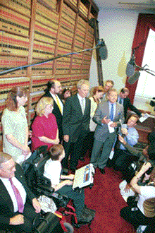 photo from a high angle of a book-lined hallway where the press kneeels before Clint Eastwood and Adapt activists look on