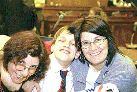 photo of Kyle with two woman friends, all their arms wrapped around each other. Kyle is of course smiling.